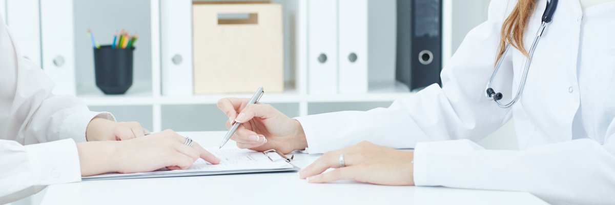 Young doctor explains how to fill out a medical form to female patient. Partnership, trust and medical ethics concept