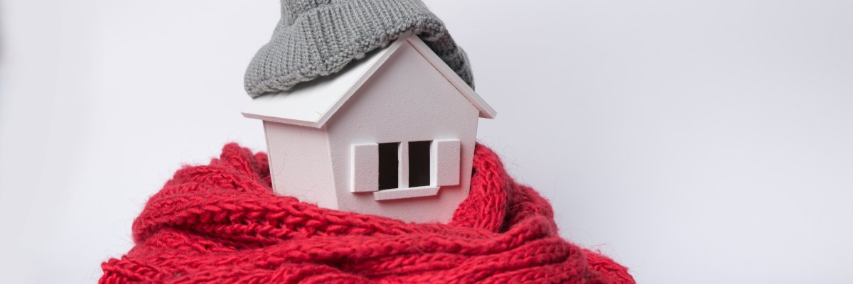 house in winter - heating system concept and cold snowy weather with model of a house wearing a knitted cap house in winter - heating system concept and cold snowy weather with model of a house wearing a knitted cap